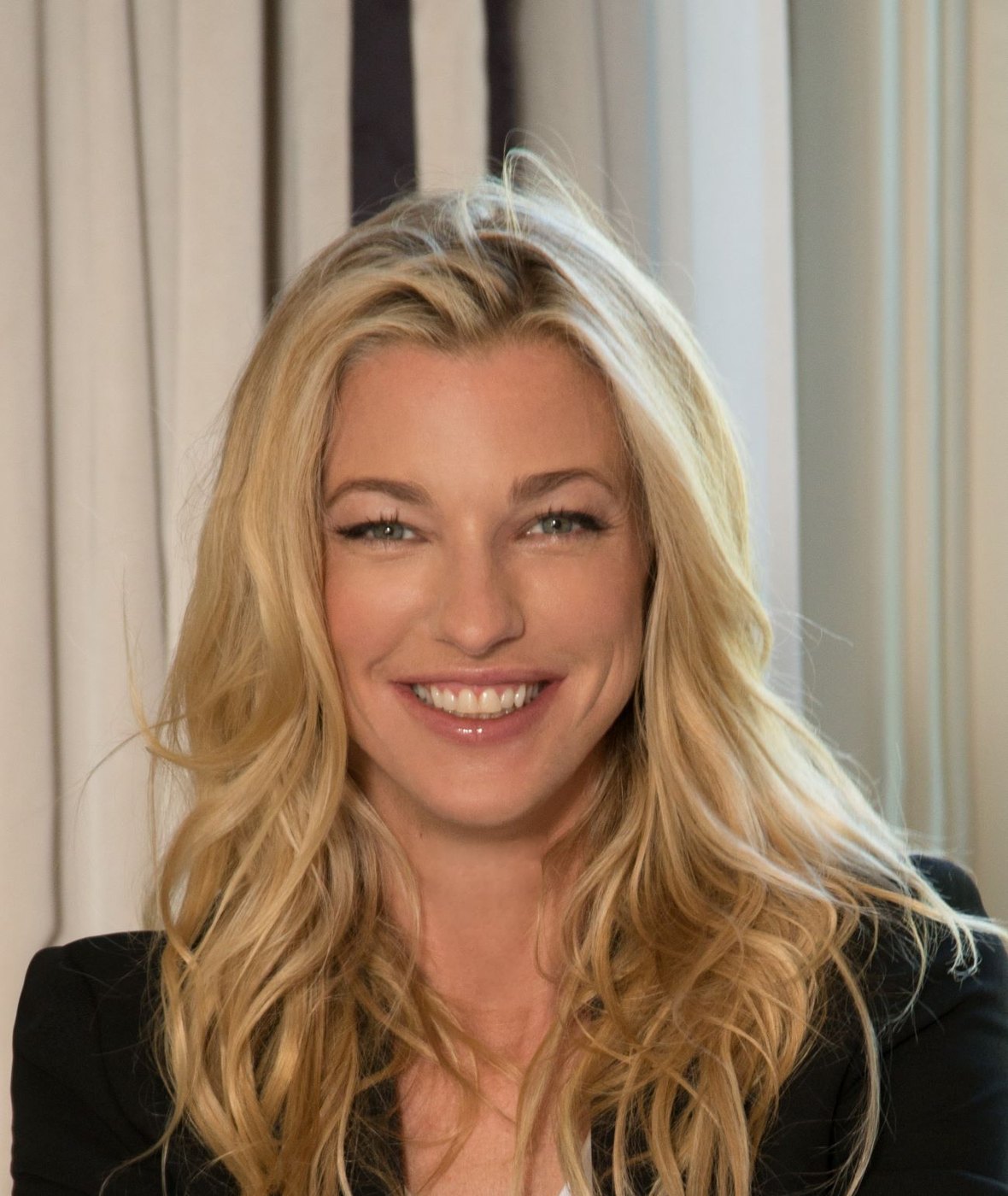 Nicole Junkerman smiling warmly in a close portrait, photographed indoors against pale curtains.